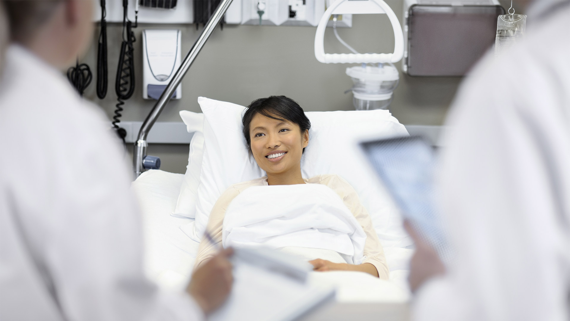 Female doctor sitting on hospital bed and discussing with young female patient