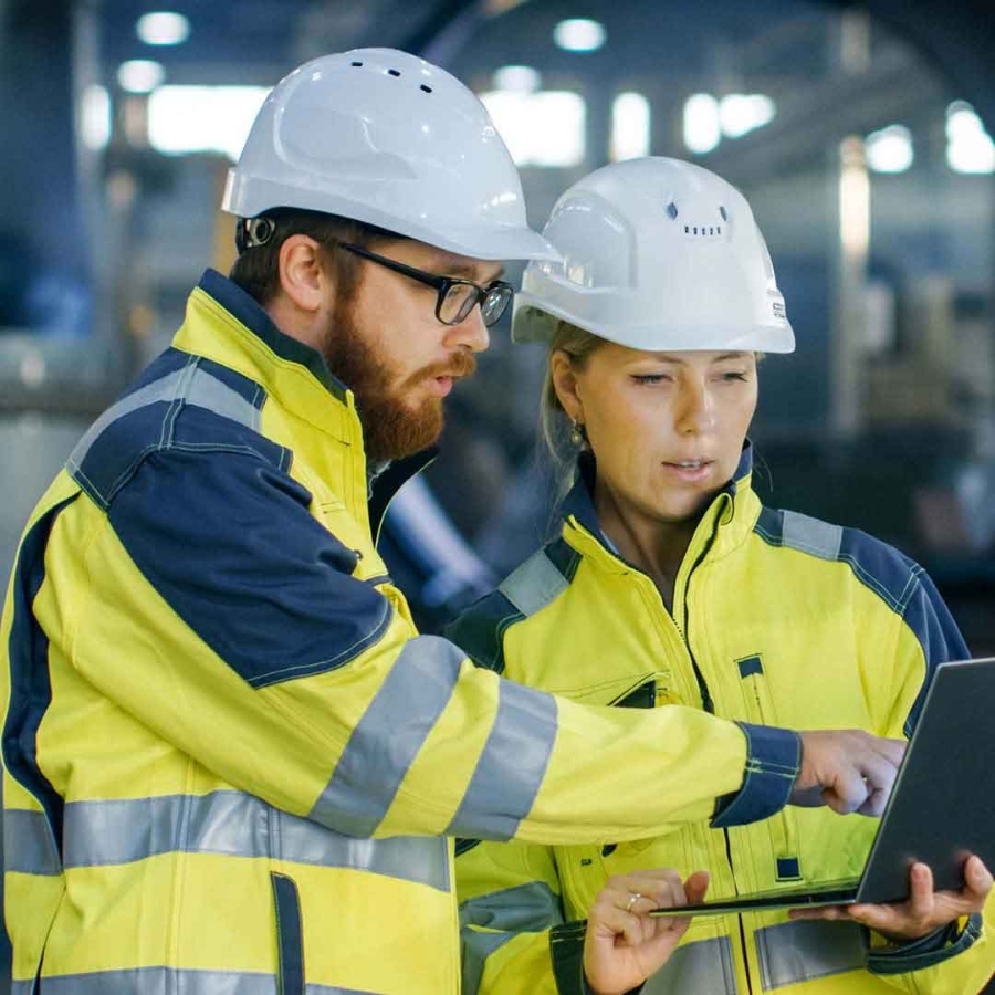 Two people wearing hard hat discussing while looking at the laptop