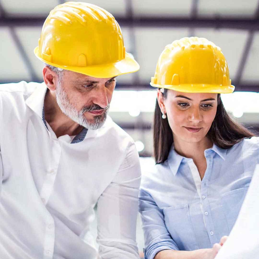 Two people wearing hard hat looking at some designs on paper